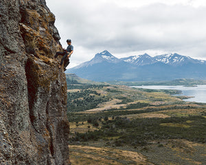 man rock climbing up a mountain face with mountains and a lake in the background